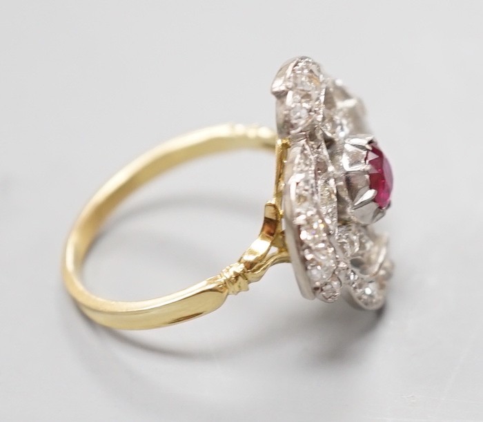 A yellow metal, ruby and diamond cluster set dress ring, in a pierced scroll setting, size O, gross weight 6 grams.